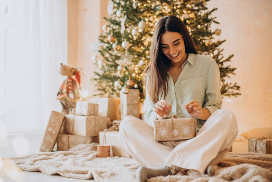 Woman in pajamas opening gifts in front of Christmas tree